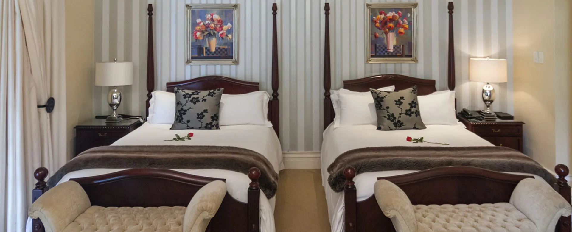 Two identical beds in a hotel room with striped wallpaper and floral paintings