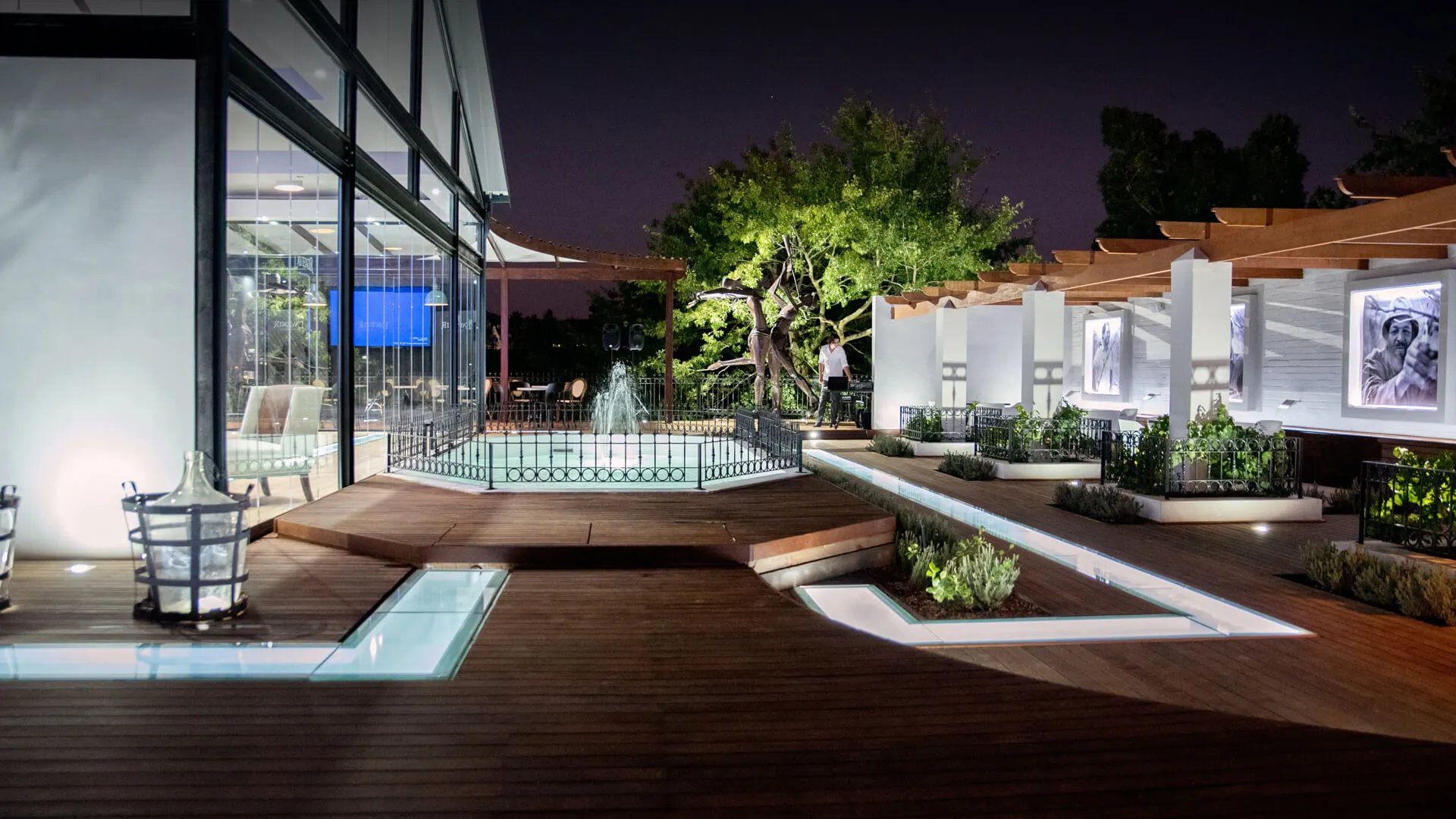 Modern outdoor patio with wooden deck illuminated planters and a central fountain