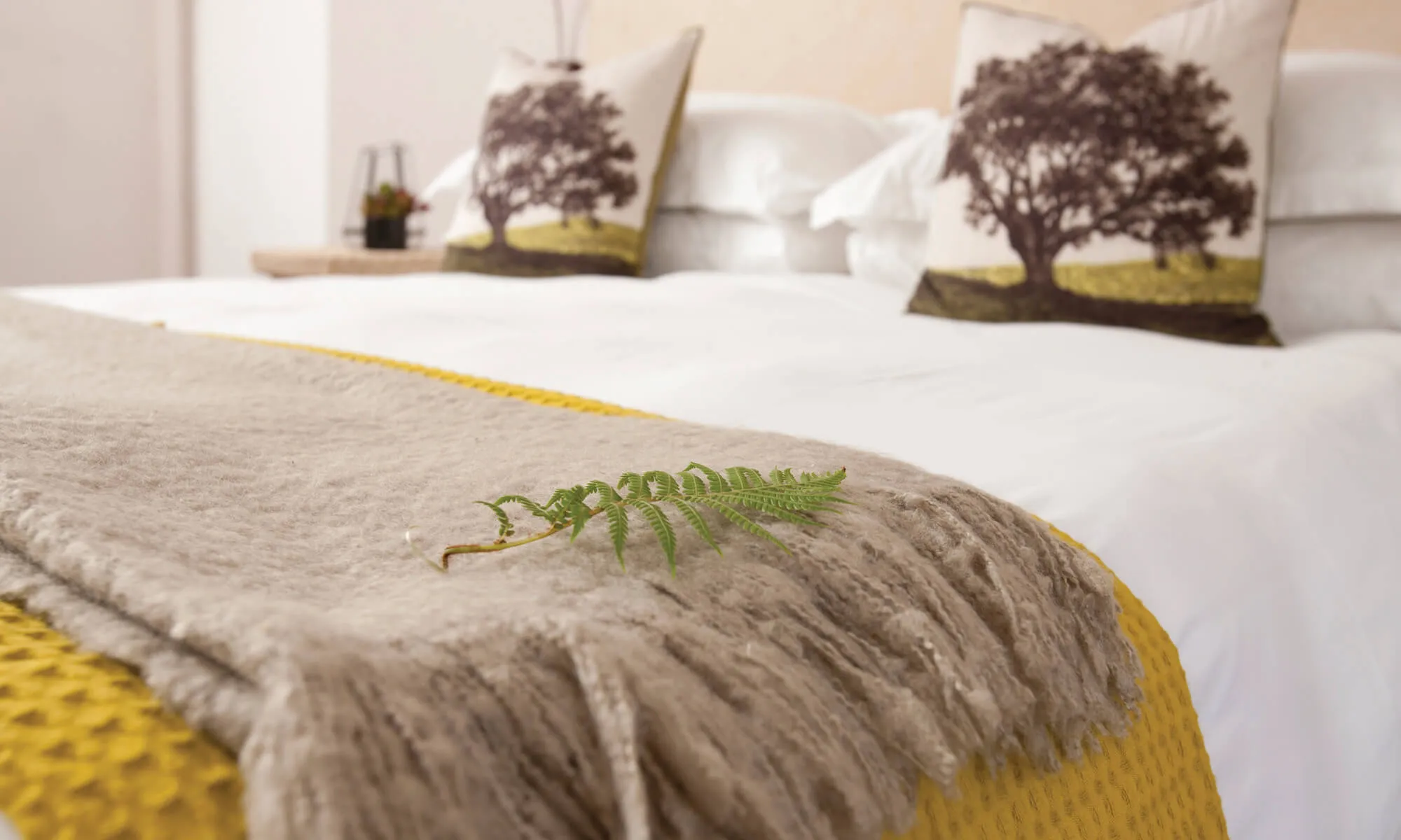 Cozy bed with beige throw green leaf and treepatterned pillows
