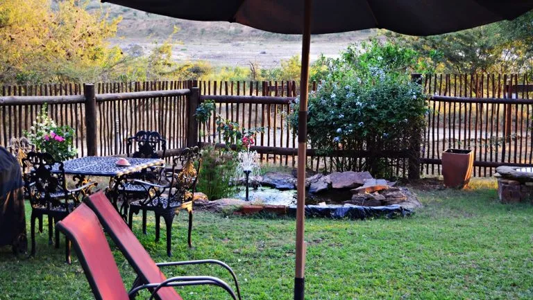 Patio with table chairs umbrella and garden area with plants and fence
