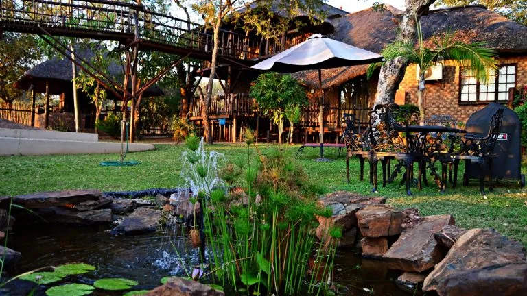 Outdoor seating area with pond plants and thatchedroof buildings in a garden