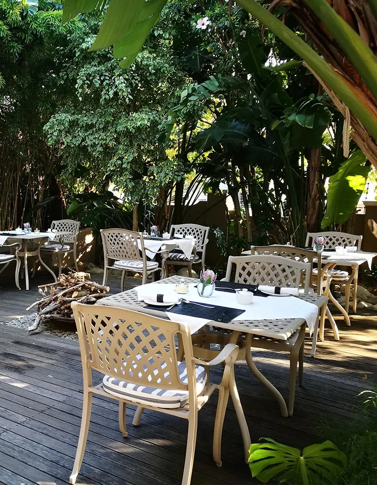 Outdoor seating area with white chairs and tables surrounded by lush greenery