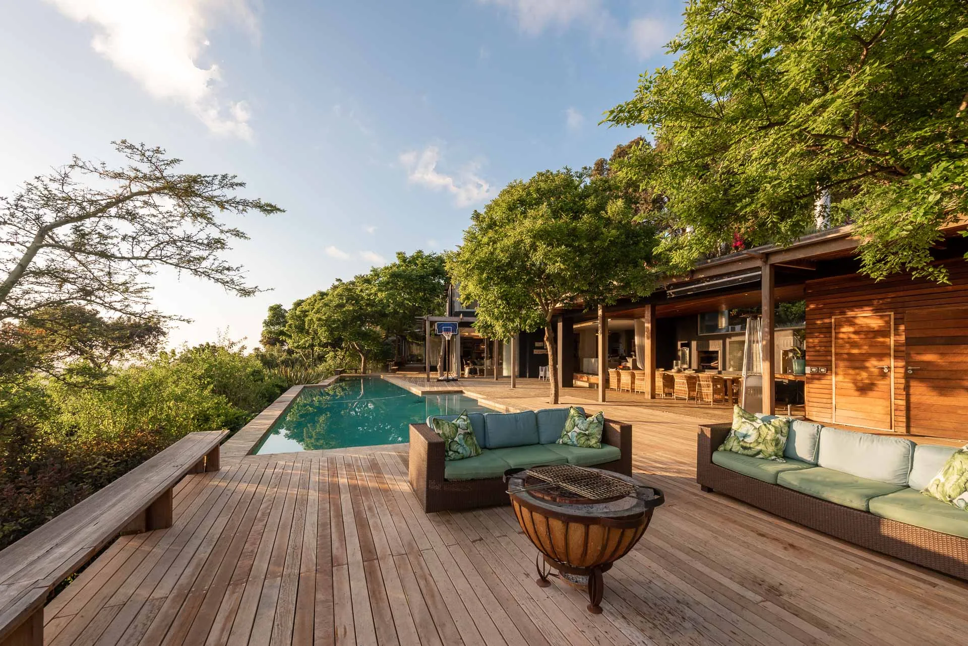 Wooden deck with pool lounge area and trees under a clear sky