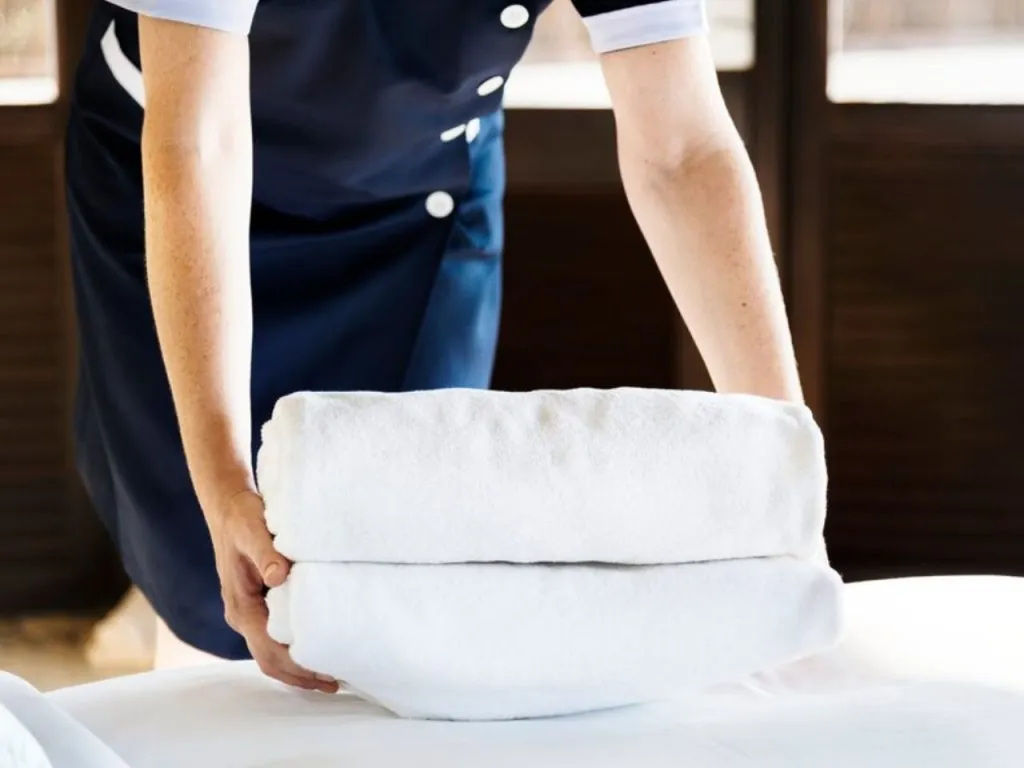 Person in uniform placing folded white towels on a surface indoors