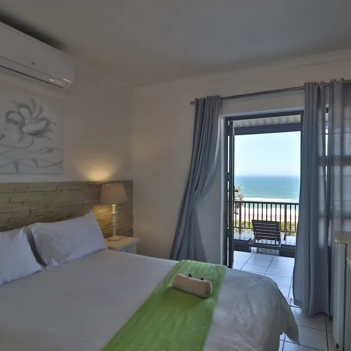 Bedroom with a bed green throw and a view of the ocean through a balcony