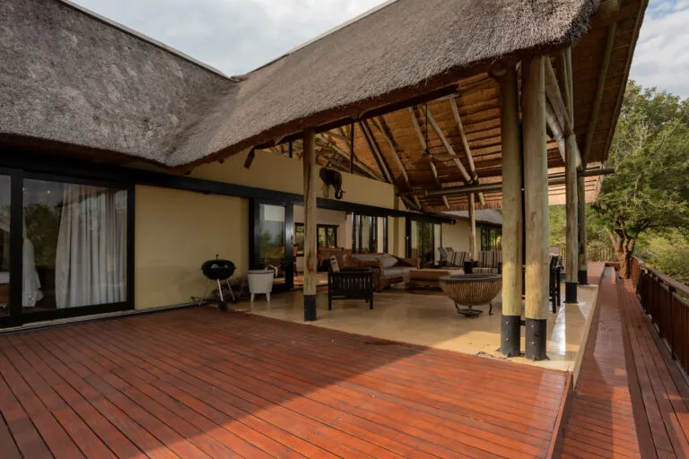Wooden deck with thatched roof outdoor furniture and large windows overlooking greenery