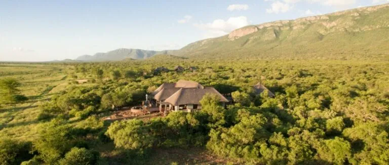Lodge with thatched roofs surrounded by lush greenery and distant mountains