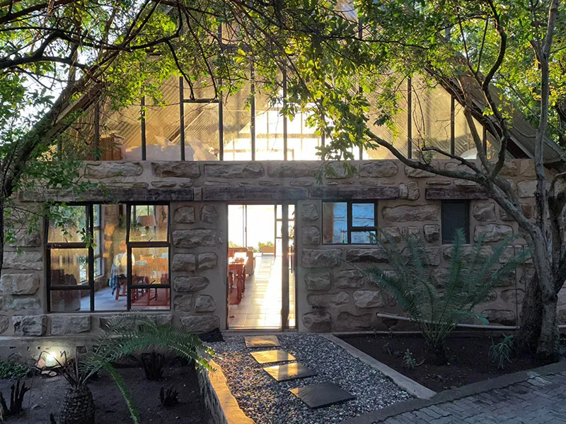 Stone house with large windows and glass roof surrounded by plants