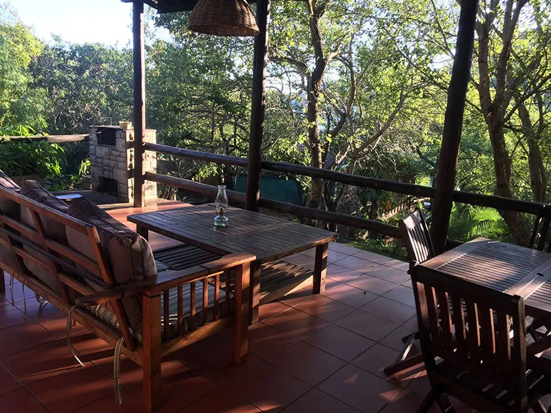 Wooden patio furniture on a tiled deck with forest view and hanging lantern