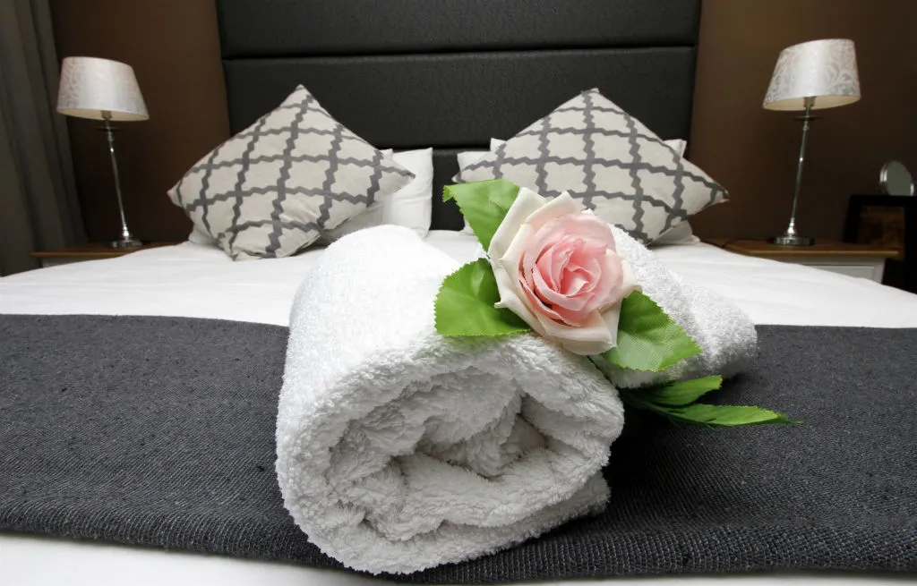 Rolled white towel with a rose on a bed with patterned pillows