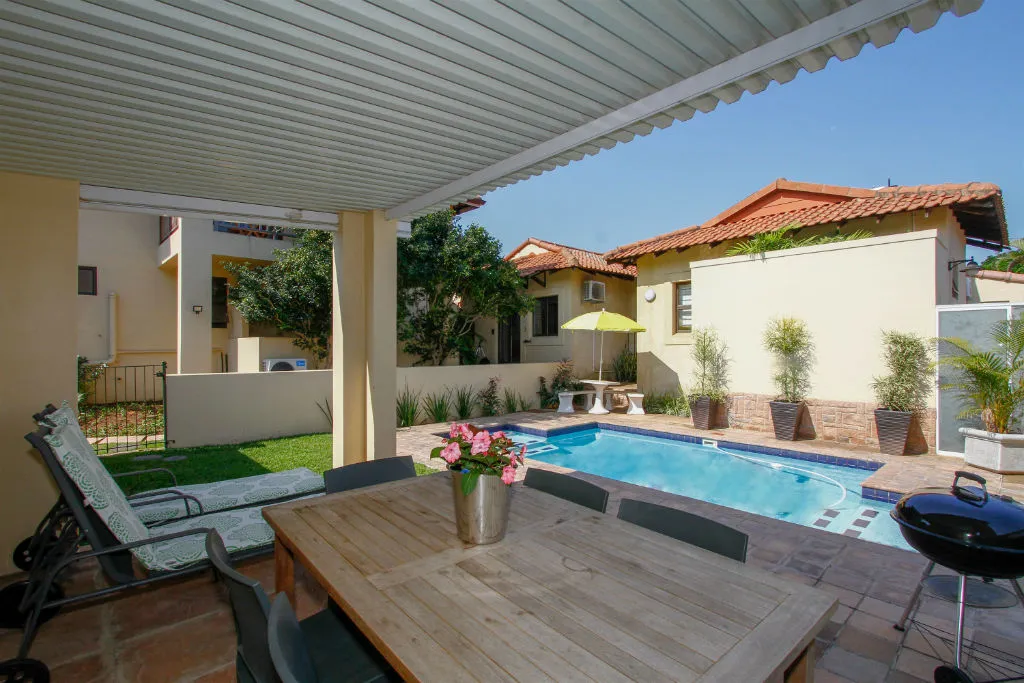 Outdoor patio with pool dining table chairs and potted plants under a pergola
