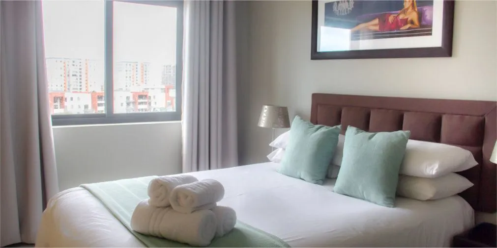 Modern bedroom with neatly made bed large window and city view