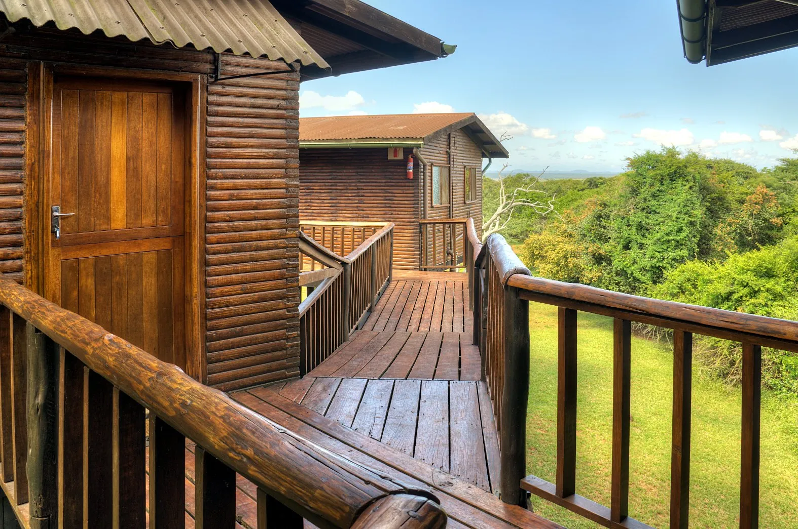 Wooden deck and walkway outside rustic cabins with green trees in the background