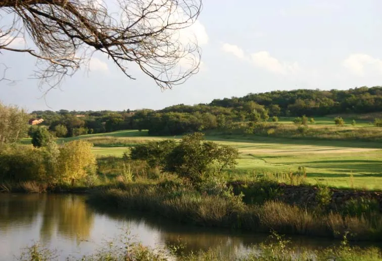Golf course with water hazard trees and rolling green landscape under blue sky