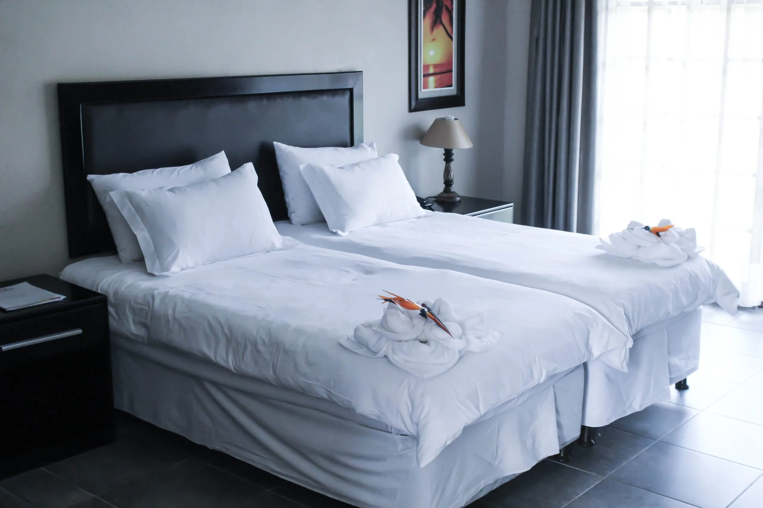 Two neatly made single beds in a modern bedroom with large windows