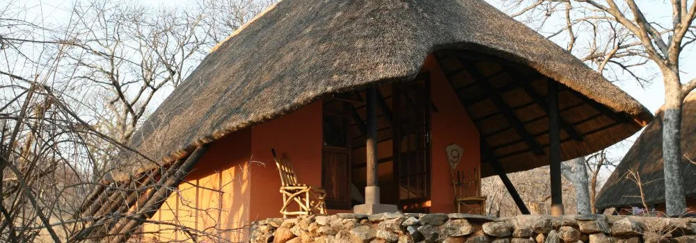 Traditional thatchedroof hut with stone wall and wooden chairs in a natural setting