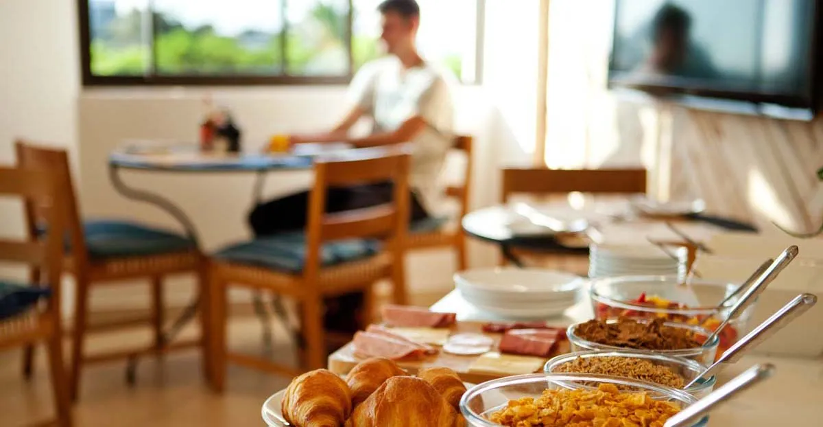 Buffet with croissants cereals and a person in the background at a table