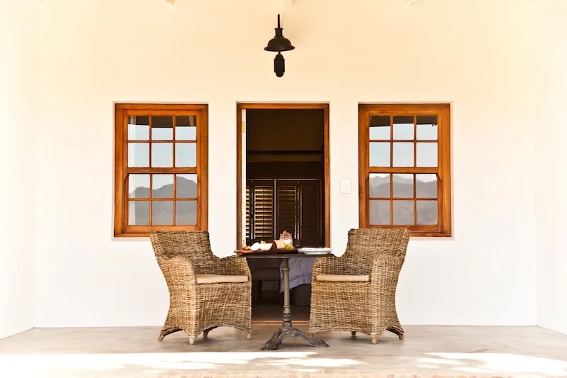 Two wicker chairs and a table outside a white building with windows and a door