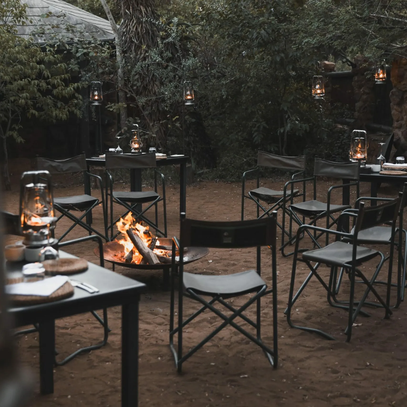 Campfire with chairs and tables in a wooded area at night