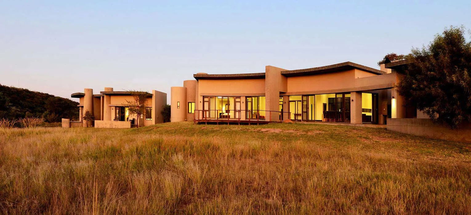 Modern house with large windows surrounded by grassy field at sunset