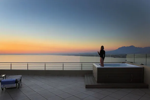 Person standing in hot tub on rooftop with ocean and sunset view