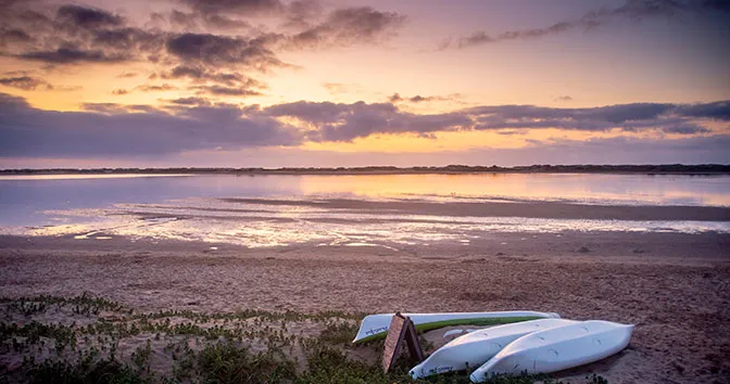 Three boats on a sandy beach at sunset with a calm sea in the background