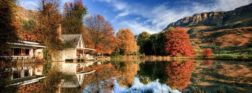 A lakeside house with autumn trees and mountains in the background