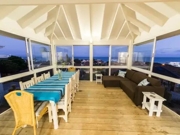 Wooden deck with dining table chairs and sofa overlooking ocean view at dusk