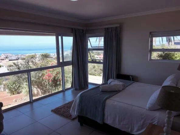 Bright bedroom with large windows overlooking the ocean neatly made bed