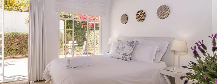 Bright bedroom with white bed large window and purple flowers on nightstand