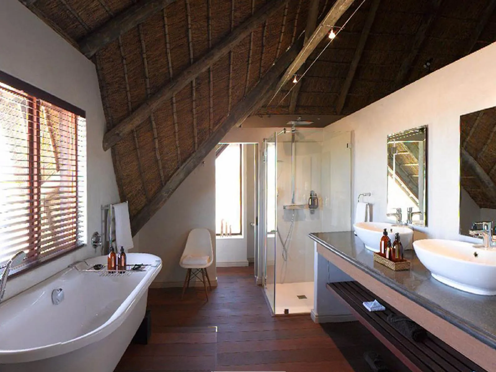 Modern bathroom with bathtub double sink and glass shower under a thatched roof