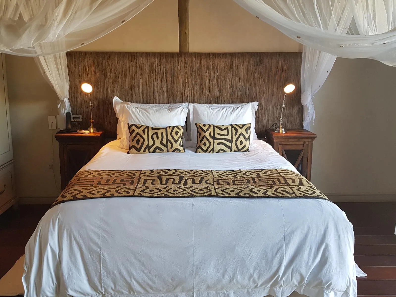Bed with patterned pillows and throw framed by a canopy and wooden headboard
