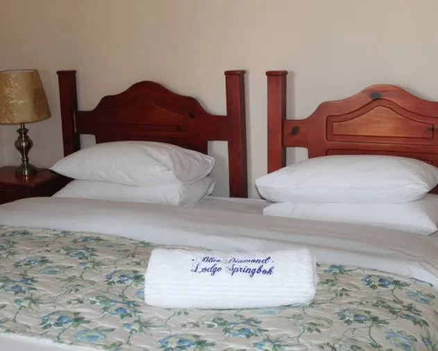Two beds with white linens and embroidered towel in a cozy bedroom