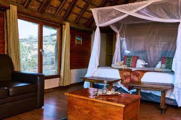 Wooden cabin bedroom with two beds under mosquito nets and large windows