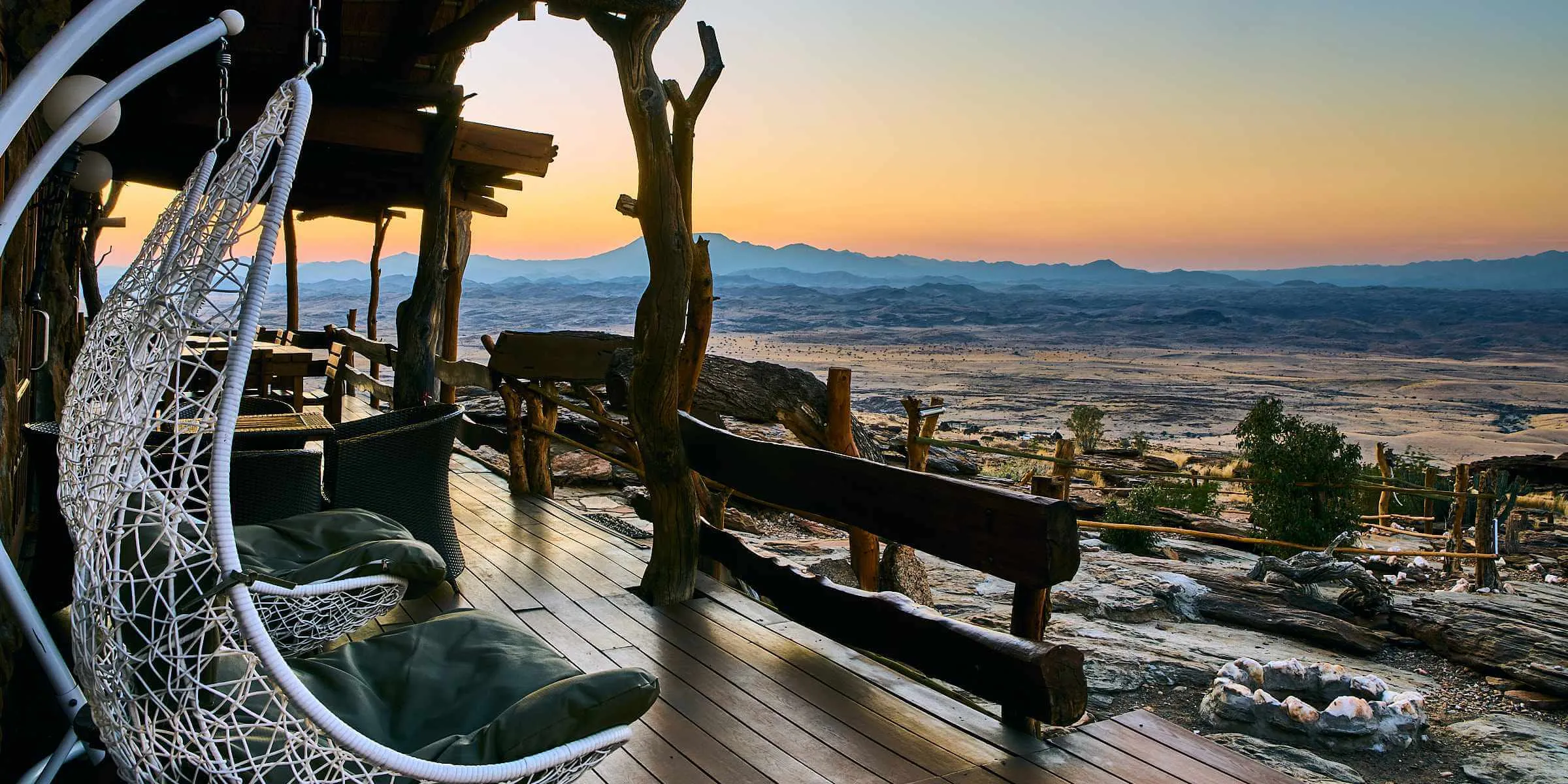 Wooden deck with hanging chairs overlooking a sunset and distant mountains