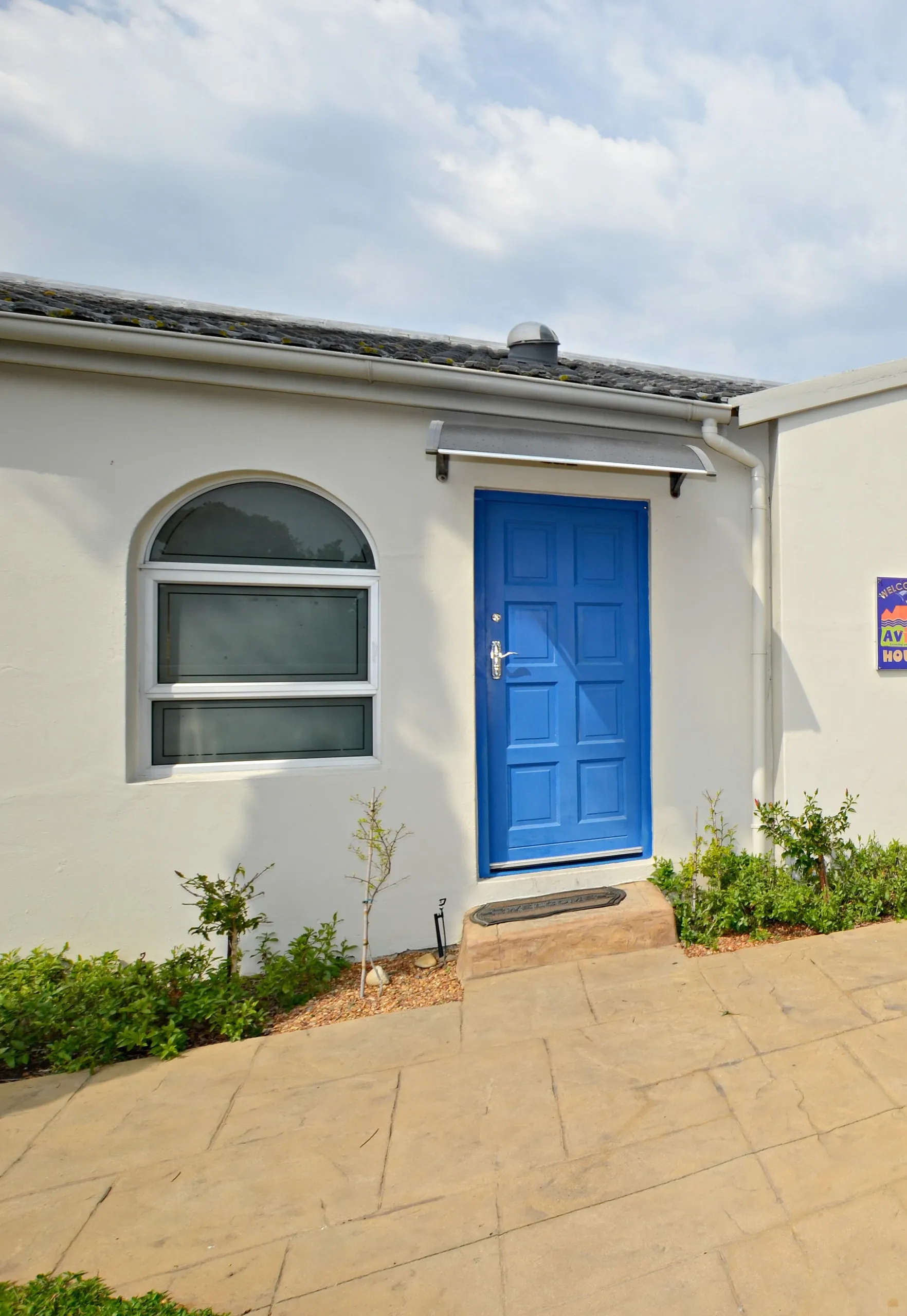 Small building with a blue door arched window and tiled pathway
