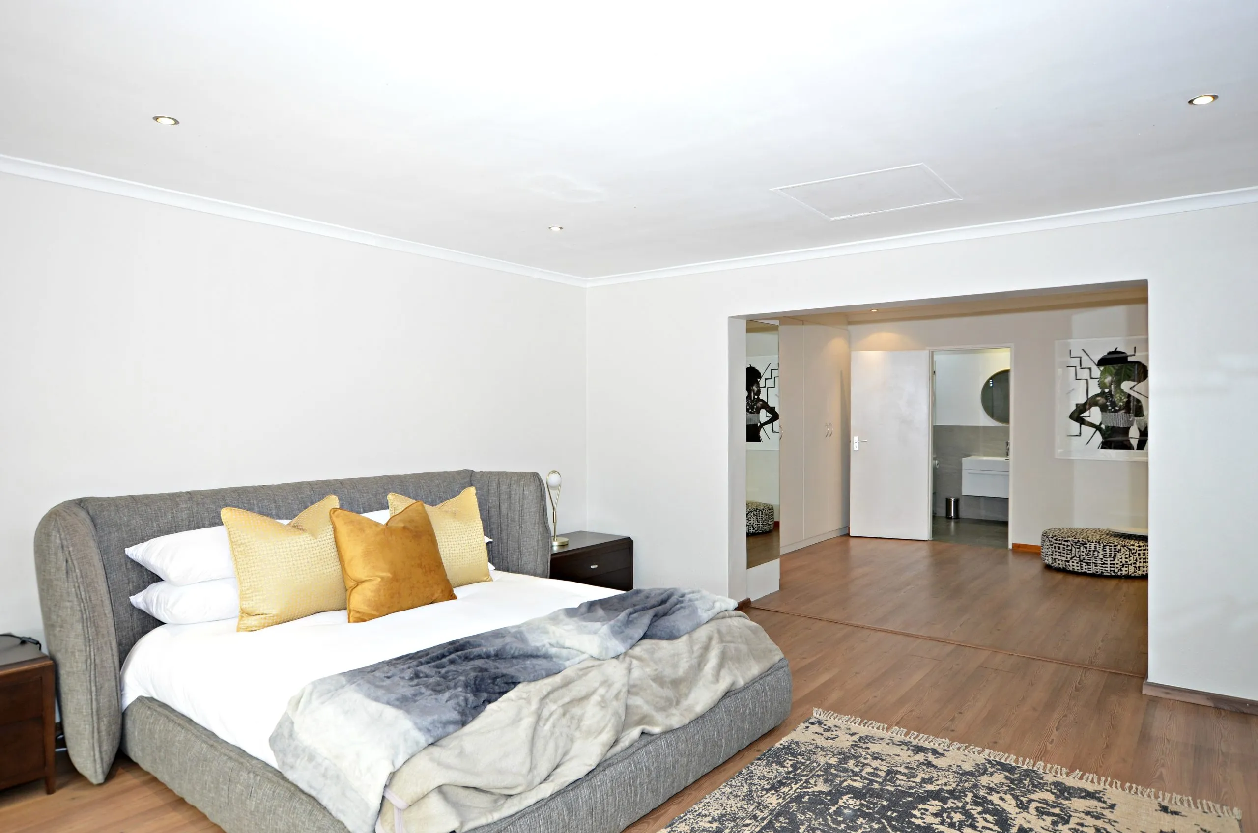 Modern bedroom with large bed pillows and wooden flooring leading to a bathroom