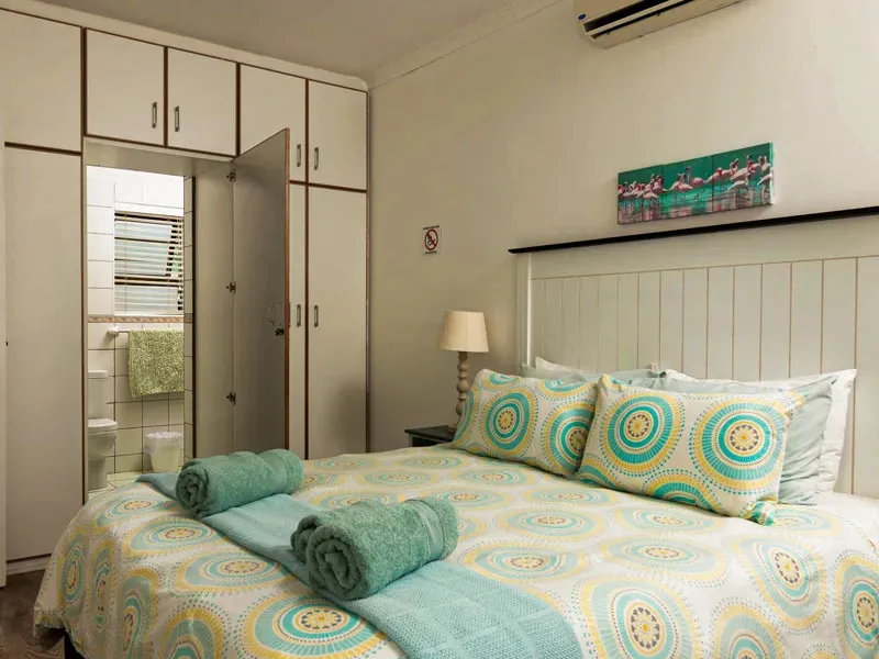 Bedroom with patterned bedspread green towels and open wardrobe revealing bathroom