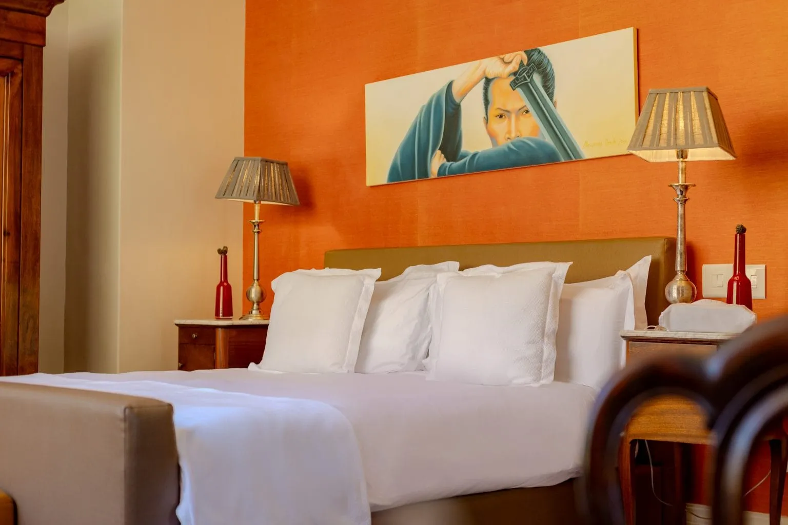 Bedroom with orange wall white bedding and a large portrait above the bed