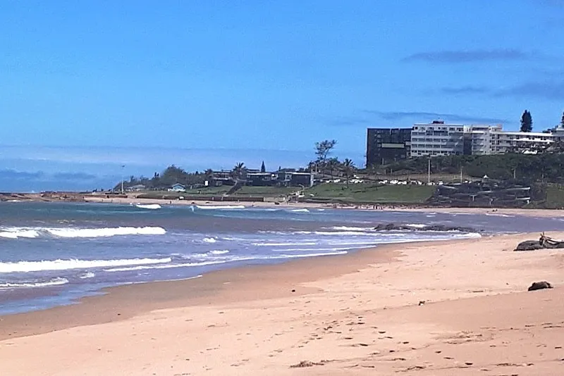 Sandy beach with gentle waves buildings and trees in the background
