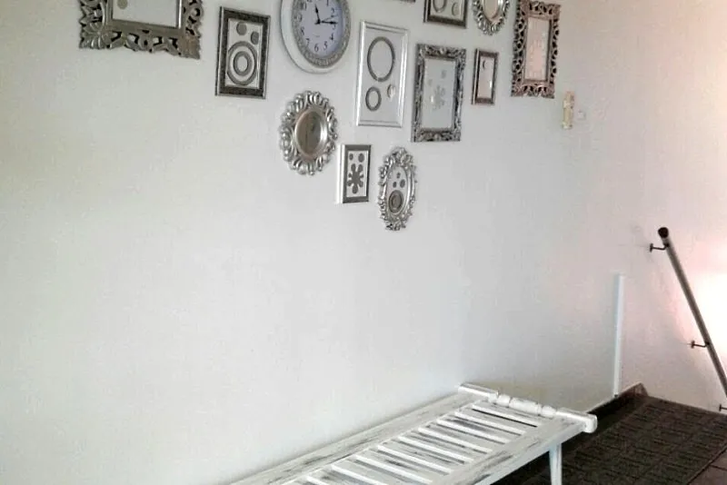 White wall with various decorative frames and a white bench below