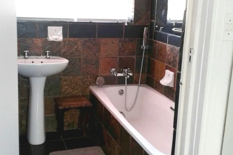 Bathroom with sink bathtub and tiled walls featuring a small wooden stool