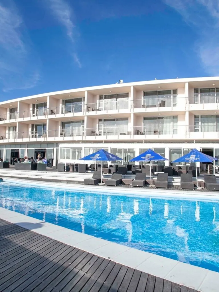 Modern hotel with pool blue umbrellas and lounge chairs under clear sky