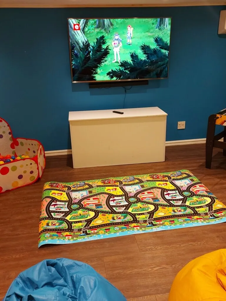 Childs playroom with TV colorful play mat and bean bags on wooden floor