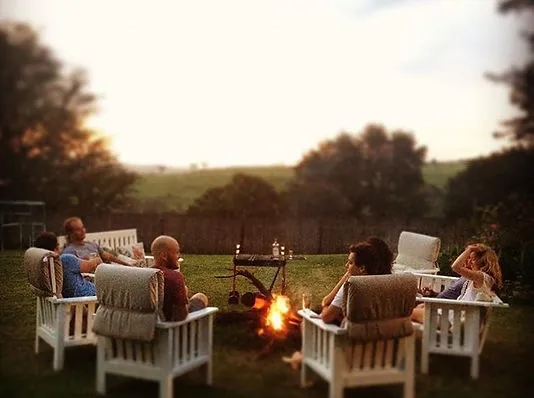 Group of people sitting around a campfire in a garden at dusk