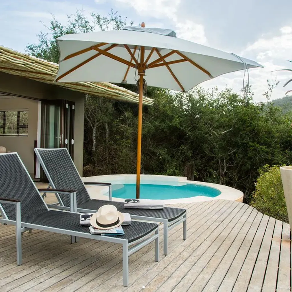 Two lounge chairs by a pool with an umbrella and hat on one chair