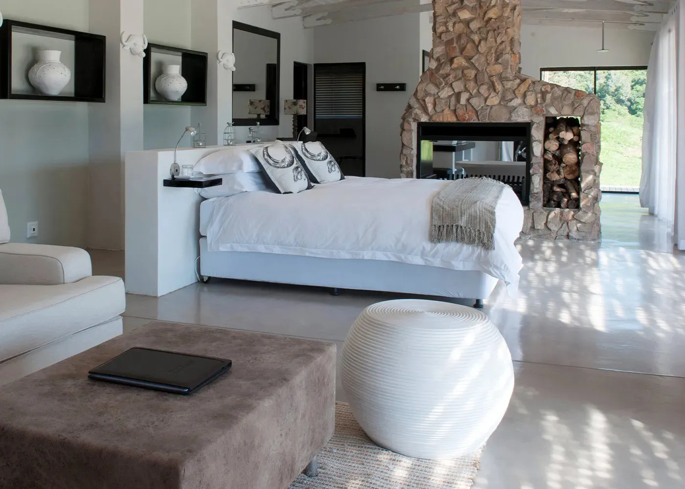 Bright bedroom with white bed stone fireplace and modern decor