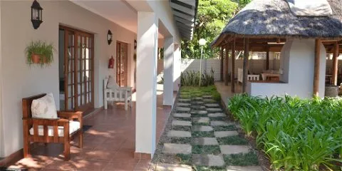 Pathway between a house and a thatchedroof structure with lush greenery