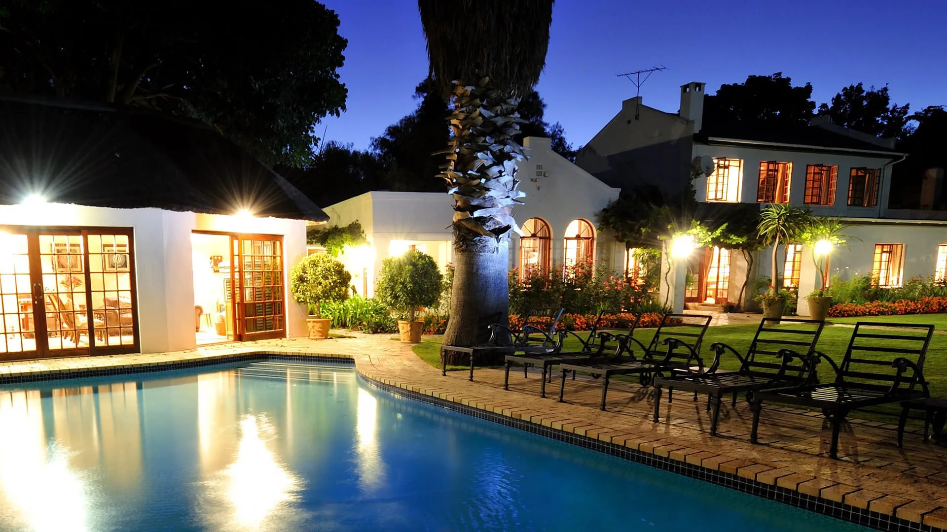 Night view of a house with a pool lounge chairs and garden lighting