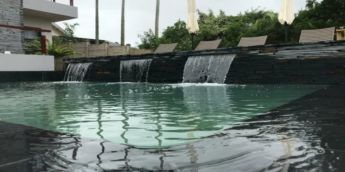 Swimming pool with cascading water features and lounge chairs in the background